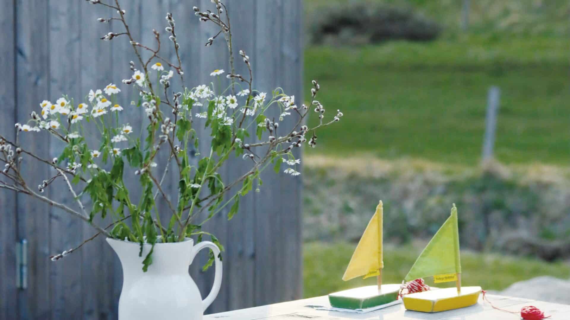 Tisch im Garten mit Wiesenblumenstrauß und zwei kleinen Segelbooten