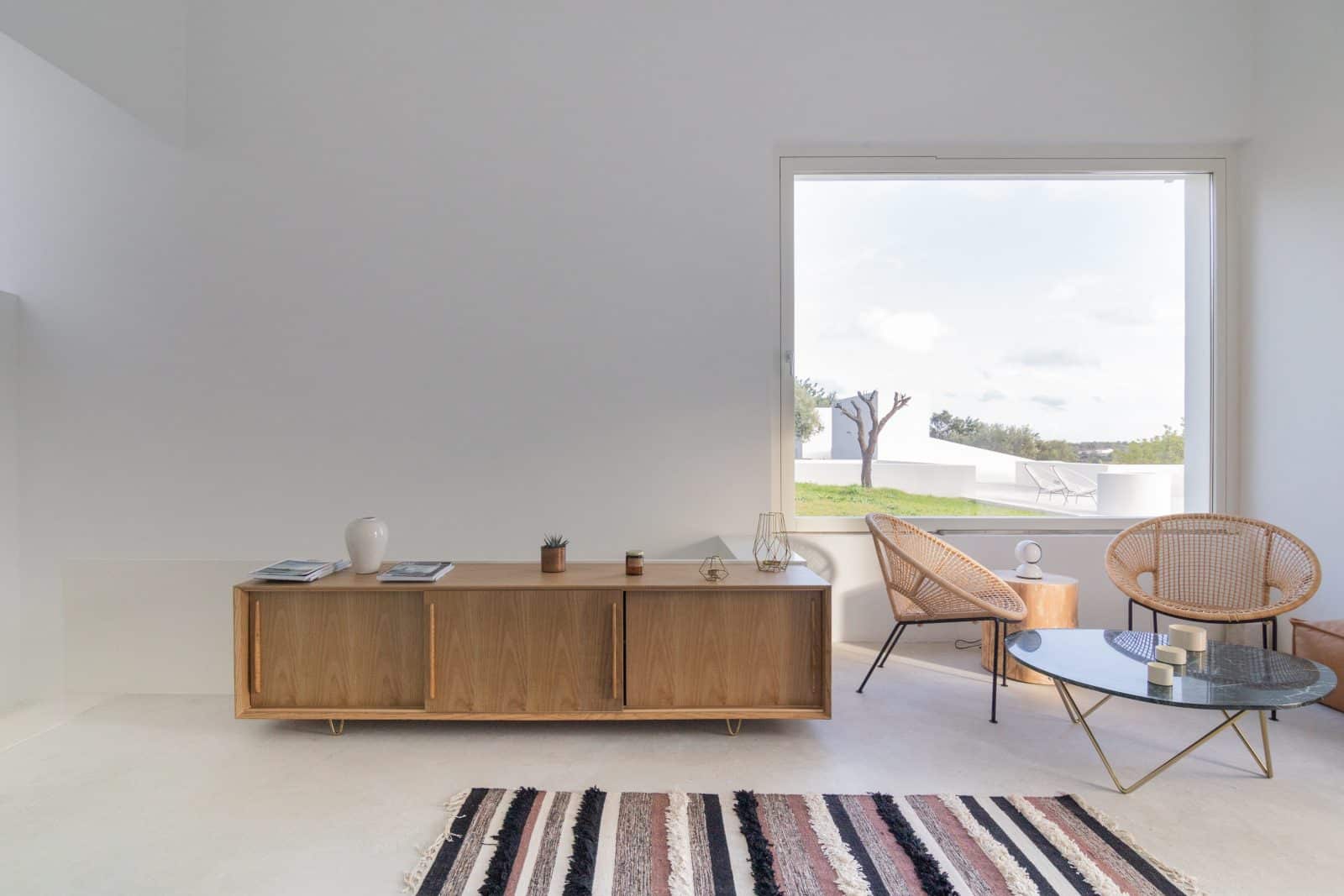 minimalistisch eingerichteter Wohnraum mit großem Fenster, Sitzplatz und Holz-Sideboard