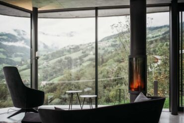 Sessel mit Ausblick aus dem großen Panoramafenster im Wohnzimmer mit Kamin im Gästehaus Freiform