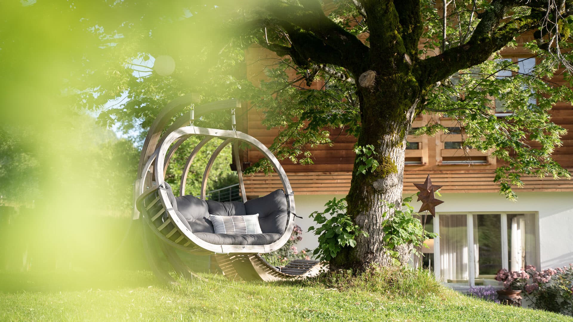 Zweipersonen-Hängesessel am Baum im Garten der Lenk Lodge