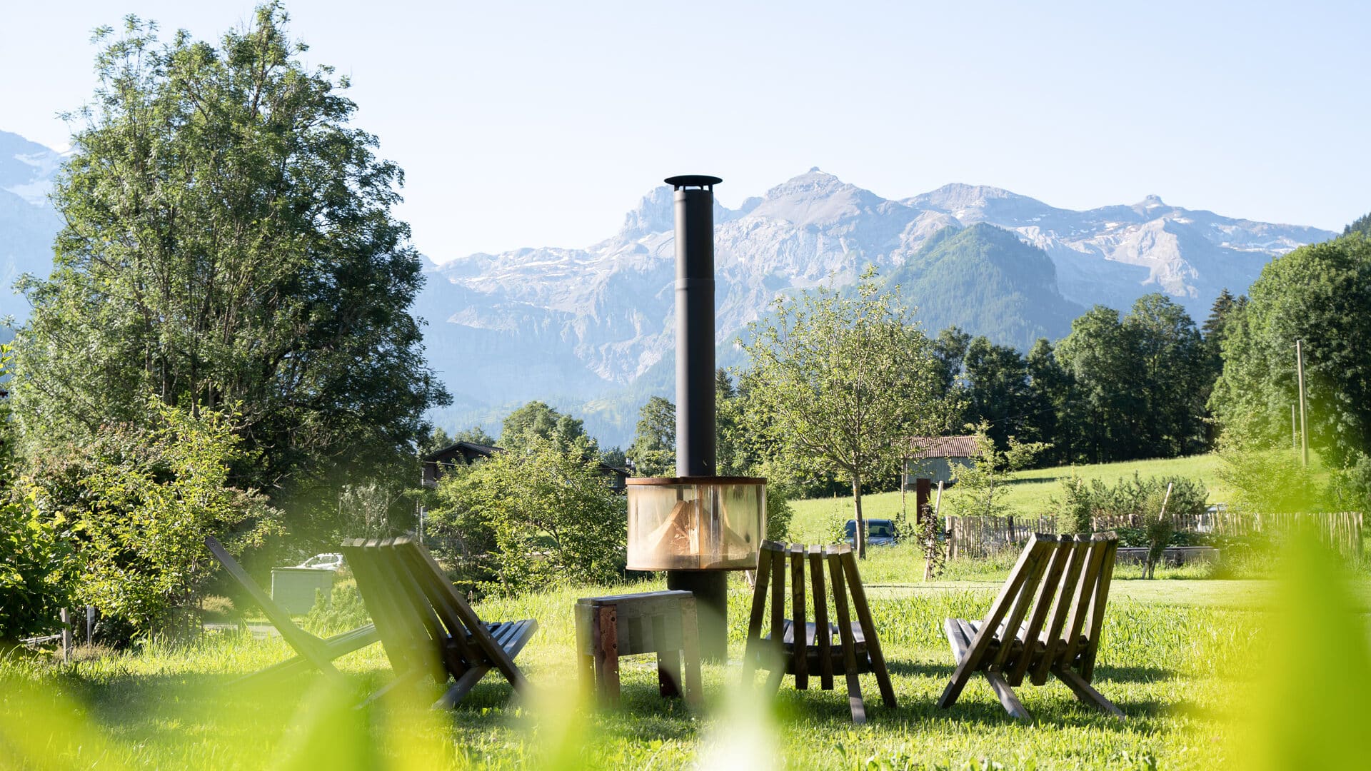 Feuerstelle mit Stühlen vor Bergkulisse im Garten der Lenk Lodge