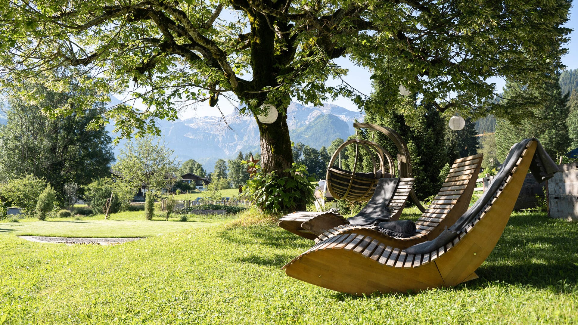 Holzliegestühle unter Baum im Garten der Lenk Lodge