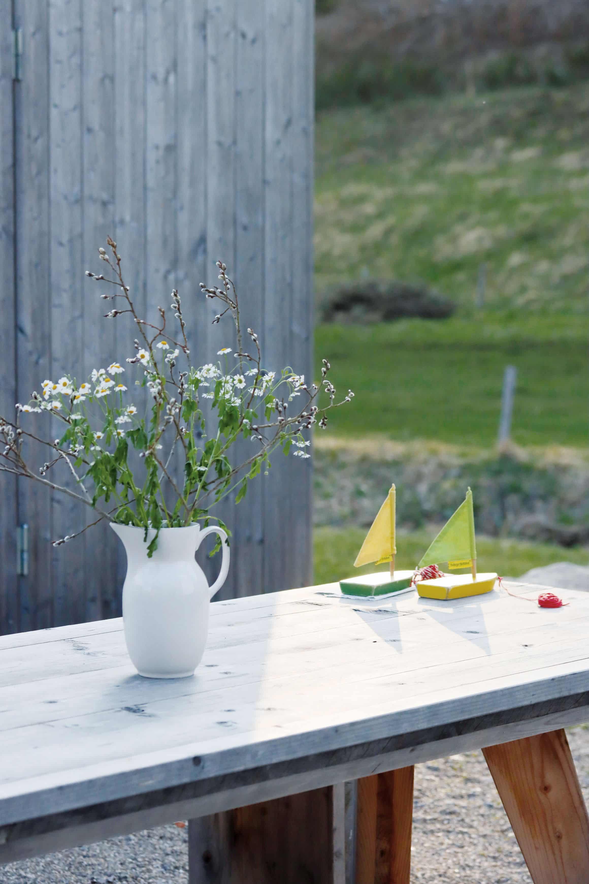 Tisch im Garten mit Wiesenblumenstrauß und zwei kleinen Segelbooten