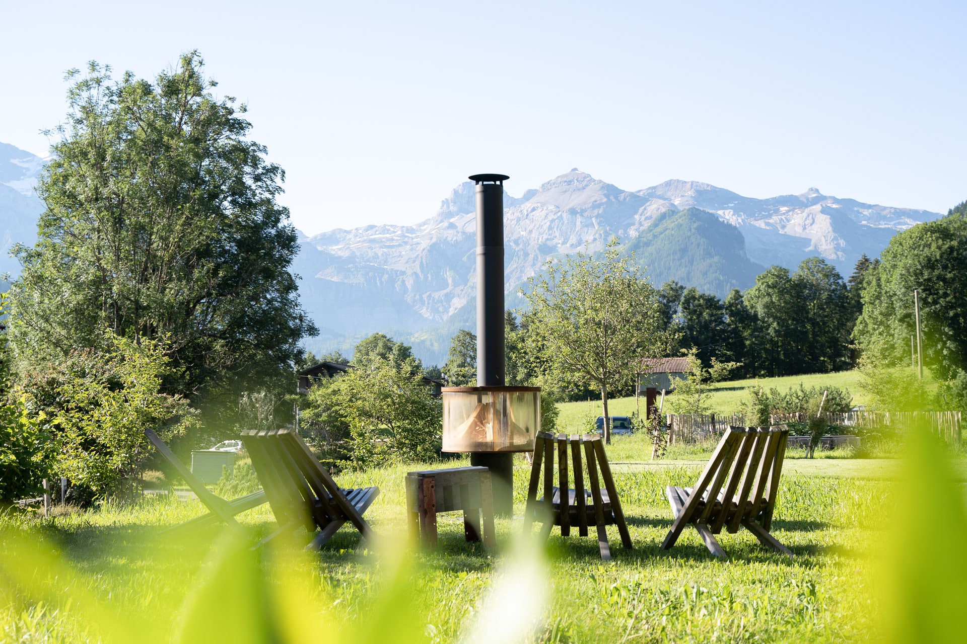 Feuerstelle mit Stühlen vor Bergkulisse im Garten der Lenk Lodge