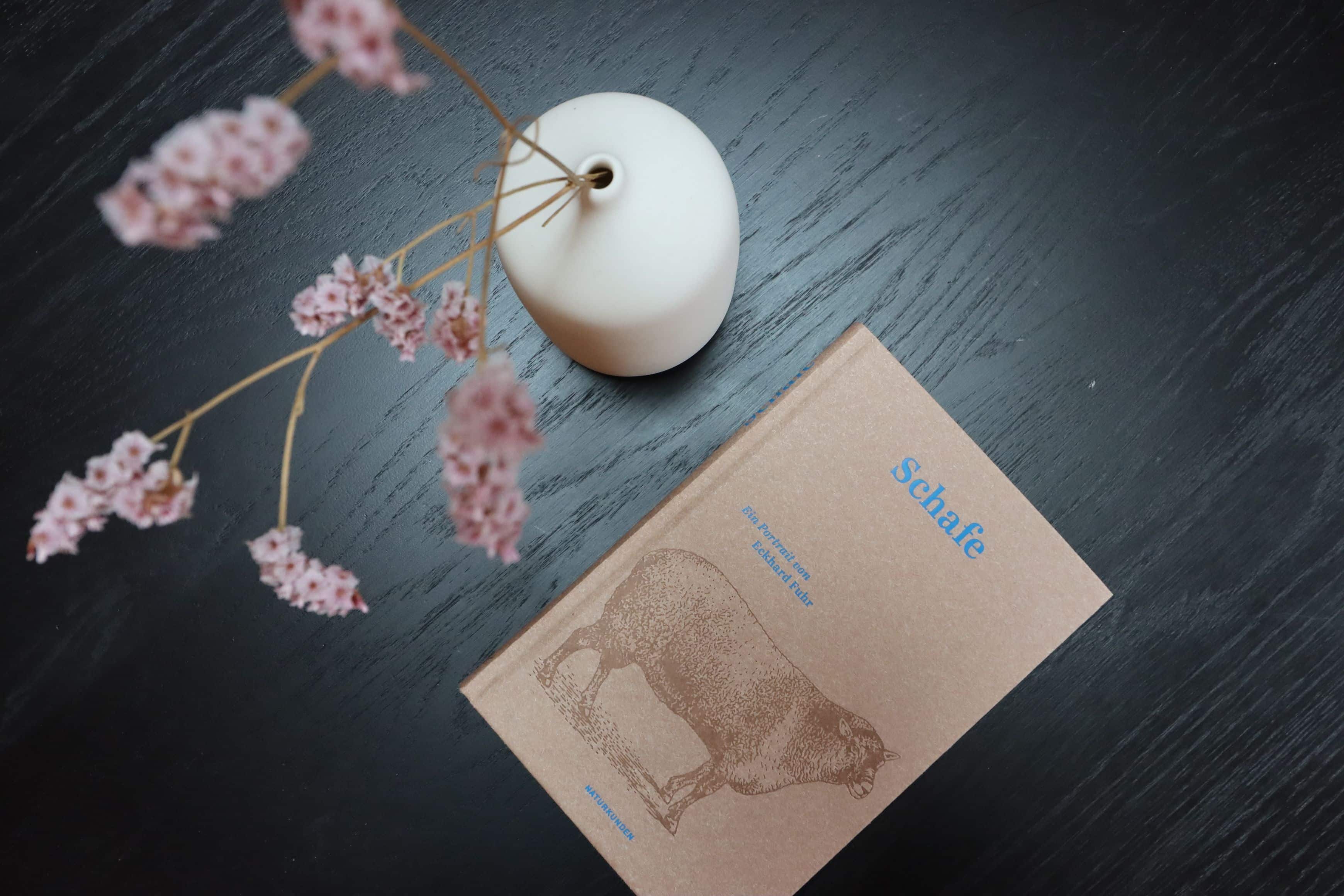 Vase und ein Buch über Schafe auf dem Tisch