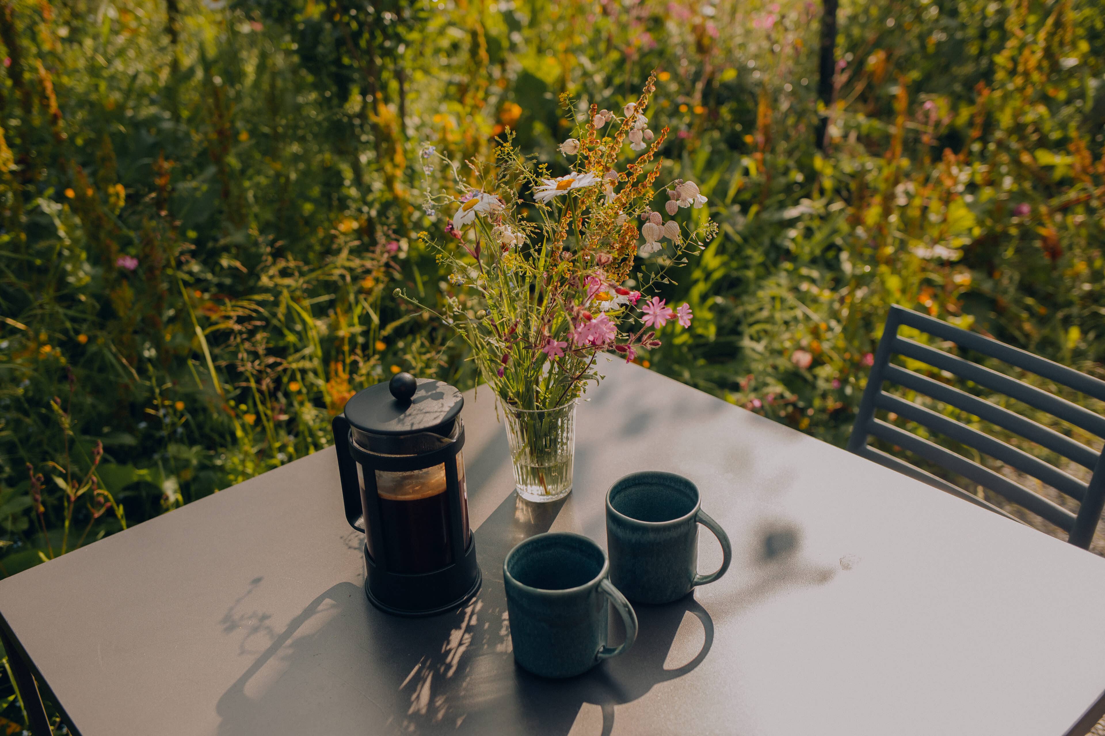 Kaffee und Blumen auf Esstisch im Freien