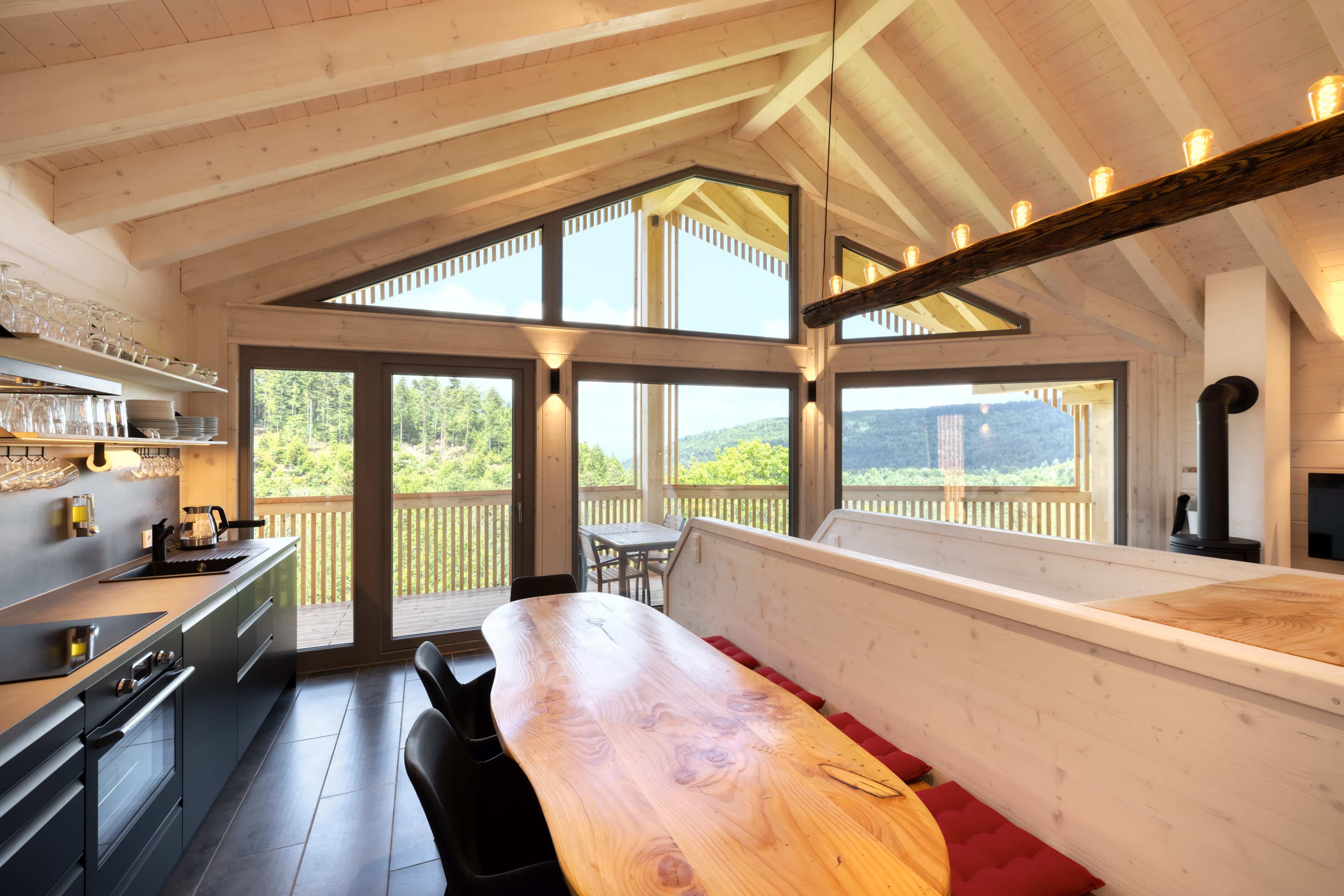 Esszimmer mit langem Holztisch, Küchenzeile und Balkon