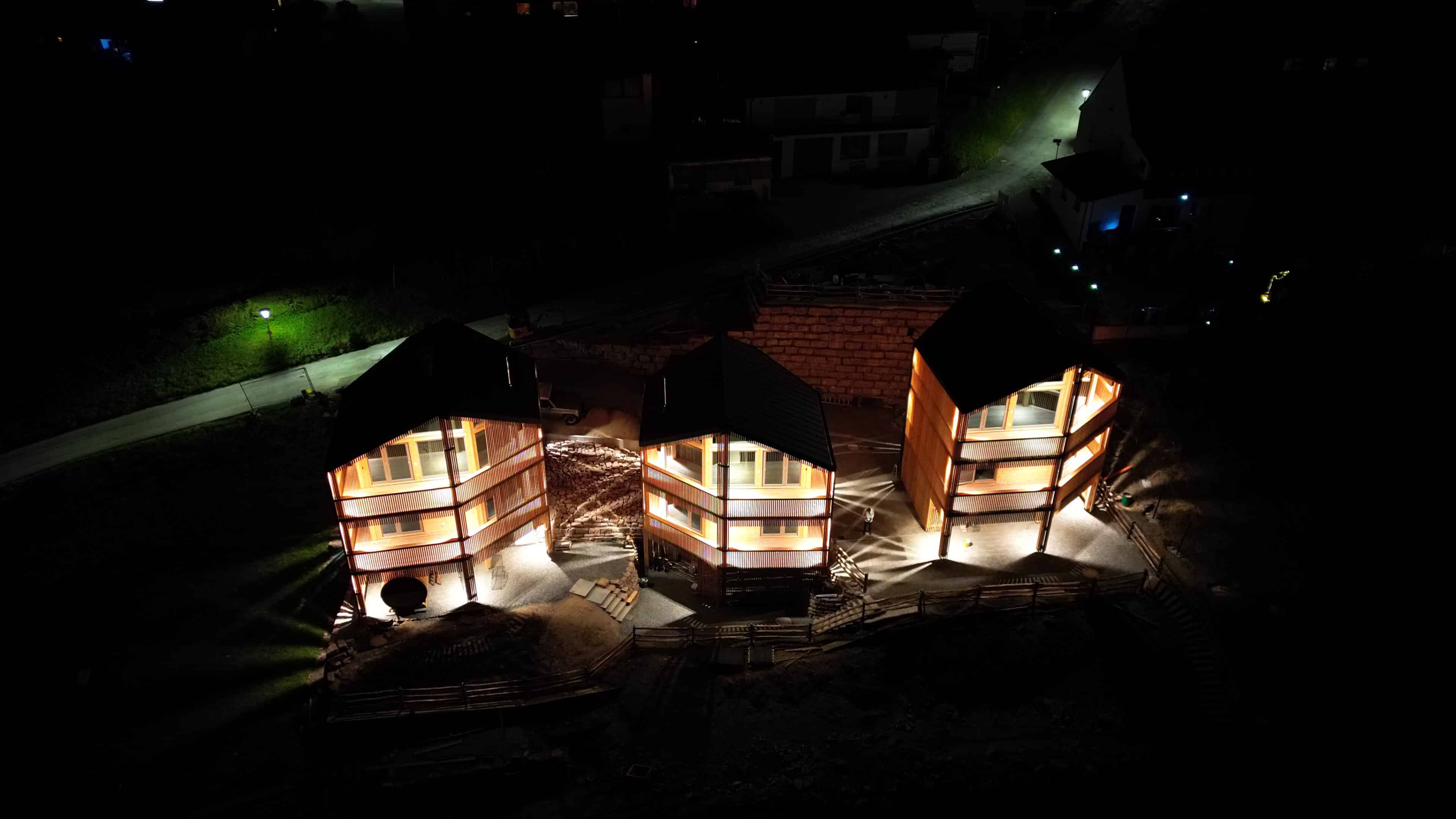 drei beleuchtete Holzhäuser aus der Vogelperspektive
