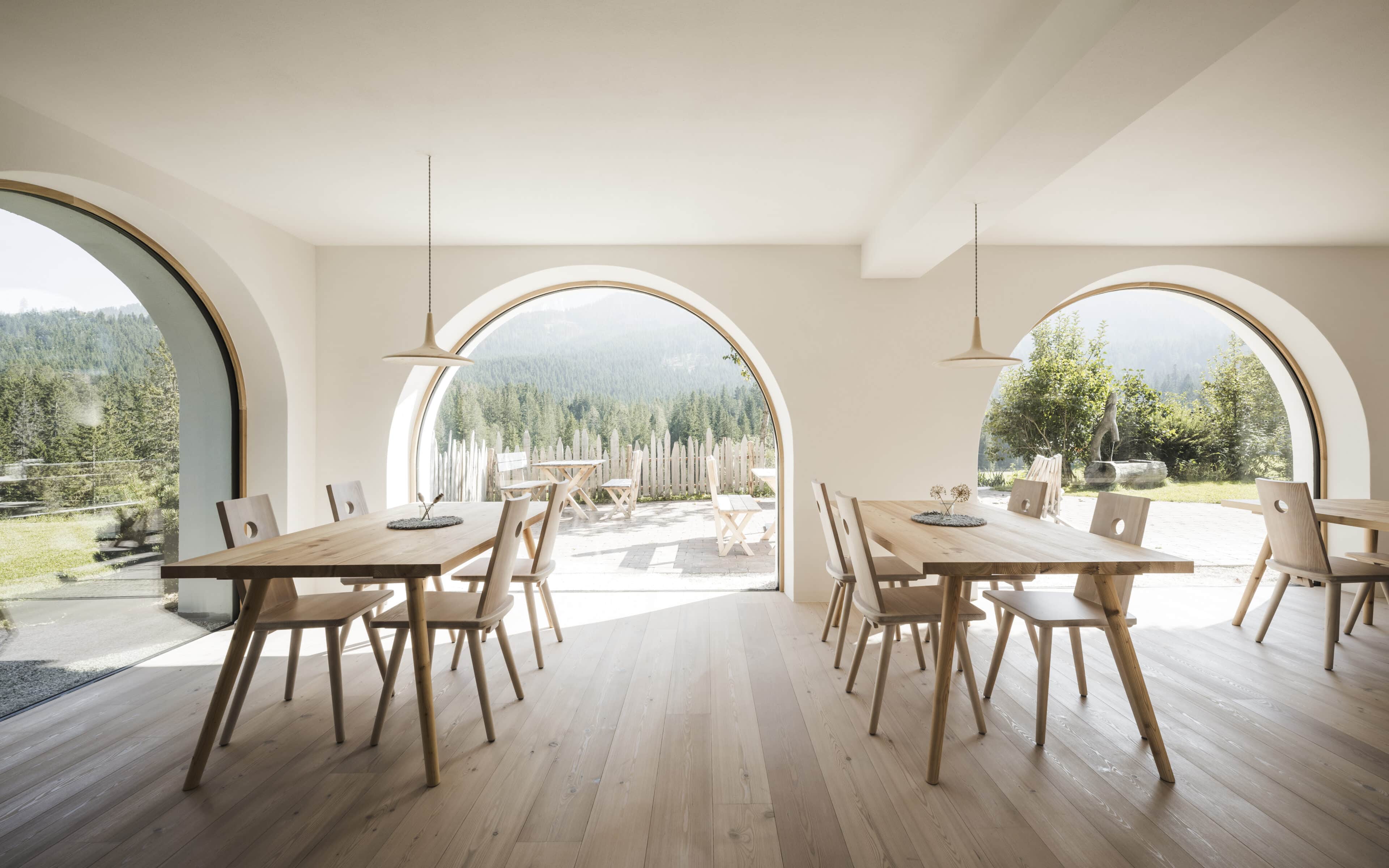 Frühstücksraum mit Holztischen und Rundbogenfenster