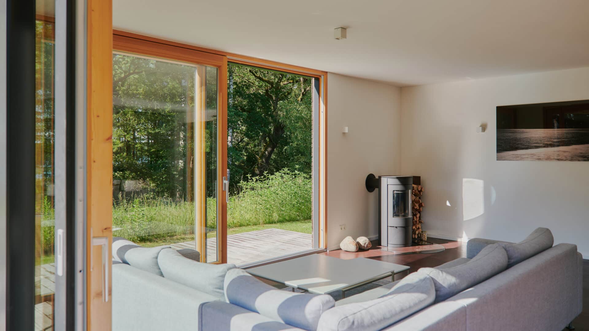 Wohnzimmerecke mit Sofa und Kamin und bodentiefen Fenstern zum Garten