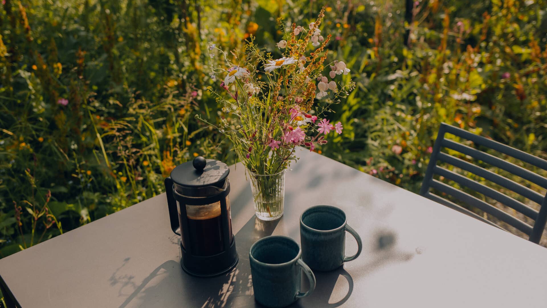 Kaffee und Blumen auf Esstisch im Freien