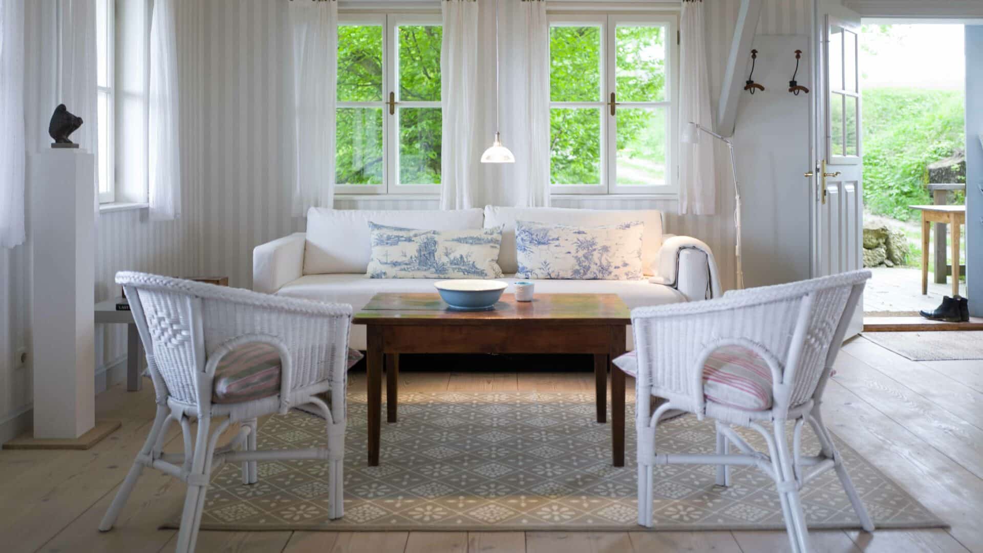Wohnraum mit Sofa und Korbstühlen und Tür zum Garten auf Hof Grillenöd